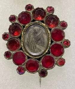 Red, circular brooch with oval in center filled with hair.